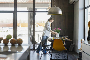 Woman arranging flower vase and setting dining table at home - SEAF02092