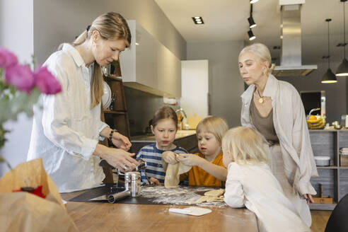 Family preparing pasta dough together at dining table - SEAF02100