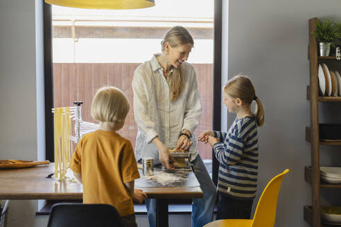 Glückliche Familie beim Schneiden von Teig in der Nudelmaschine zu Hause - SEAF02111