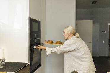 Ältere Frau öffnet den Ofen, um zu Hause Brot zu backen - SEAF02119