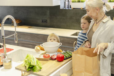 Grandmother with granddaughter and grandson preparing food at home - SEAF02128