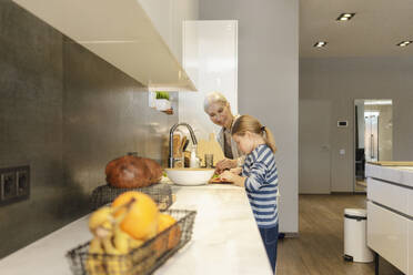 Happy grandmother with granddaughter preparing food in kitchen at home - SEAF02130