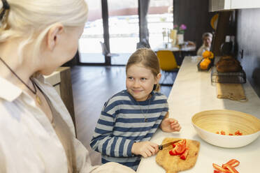 Happy girl cutting red bell pepper with grandmother in kitchen at home - SEAF02131