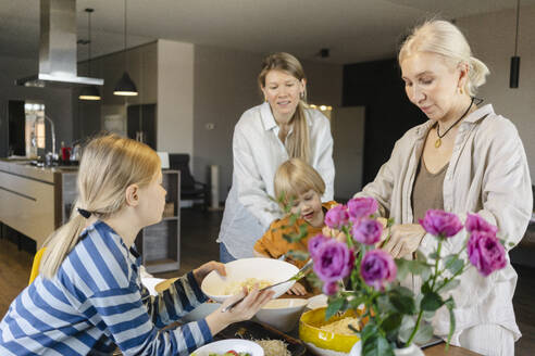 Grandmother serving food to family at dining table at home - SEAF02148