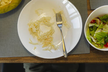 Weißer Teller mit Spaghetti neben Schüssel mit Salat auf dem Tisch - SEAF02150