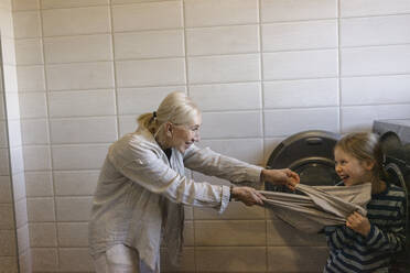 Großmutter zieht an einem Tuch und hat Spaß mit ihrer Enkelin im Badezimmer - SEAF02152
