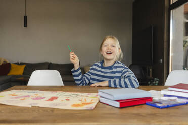 Glückliches Mädchen, das einen Bleistift hält und mit einer Zeichnung am Schreibtisch sitzt - SEAF02158