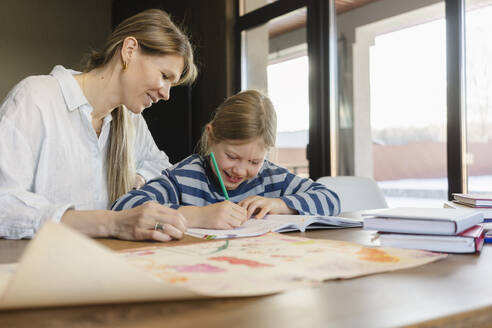 Smiling mother helping daughter doing homework at desk - SEAF02160