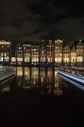 Illuminated buildings near river at night in Amsterdam city - JCCMF10991