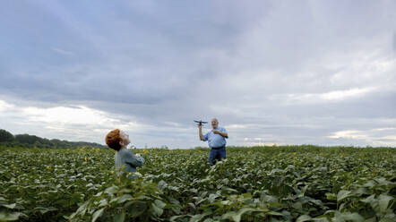 Grandfather and grandson playing with toy airplane in field - MBLF00197