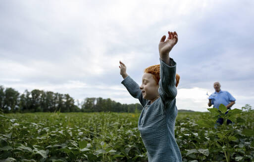 Fröhlicher Junge läuft mit Großvater im Hintergrund auf einem Feld - MBLF00199