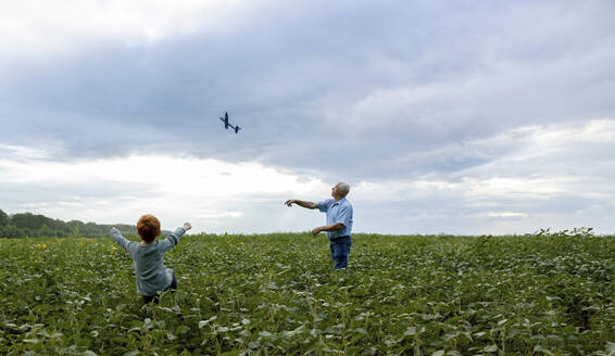 Grandfather and grandson flying toy airplane in field - MBLF00201