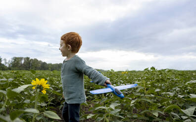 Rothaariger Junge spielt mit Spielzeugflugzeug auf einem Feld - MBLF00202