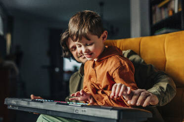 Lächelnder Vater bringt seinem Sohn zu Hause das Spielen auf dem E-Piano bei - VSNF01537