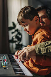 Father holding hands and teaching electric piano to son at home - VSNF01538