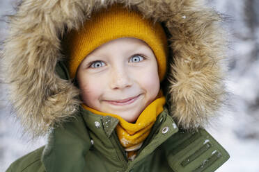 Lächelnder süßer Junge mit Parka-Jacke im Schnee - NJAF00719