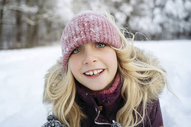 Lächelndes blondes Mädchen mit Strickmütze im Winter - NJAF00725