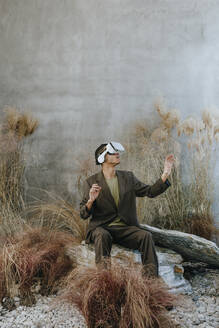 Geschäftsmann gestikuliert mit Virtual-Reality-Simulator und sitzt auf einem Felsen im Garten - YTF01506
