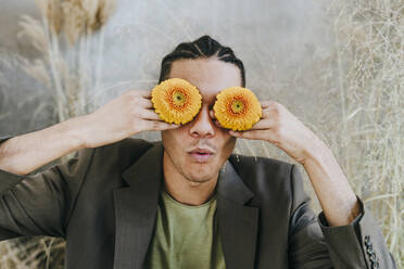 Businessman covering eyes with Gerbera daisies in garden - YTF01524