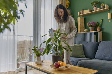 Junge Frau, die sich um eine Pflanze auf dem Couchtisch zu Hause kümmert - SECF00049