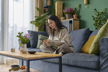 Frau mit Smartphone im Schneidersitz auf dem Sofa zu Hause - SECF00053