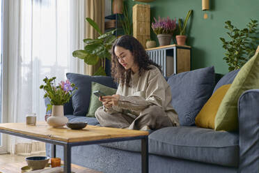 Woman using smart phone sitting cross-legged on sofa at home - SECF00053