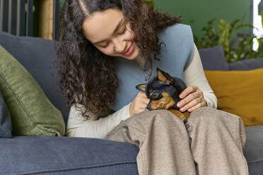 Lächelnde Frau streichelt Chihuahua, der zu Hause auf dem Sofa sitzt - SECF00058