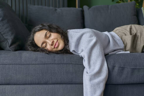 Smiling woman lying down on sofa with eyes closed at home - SECF00059