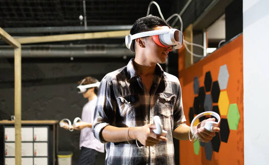 Seitenansicht eines jungen, aufgeregten Mannes, der mit einem VR-Headset und Controllern ein Virtual-Reality-Spiel spielt - ADSF50474