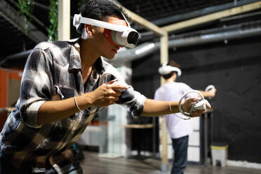 Seitenansicht eines jungen, aufgeregten Mannes, der mit einem VR-Headset und Controllern ein Virtual-Reality-Spiel spielt - ADSF50481