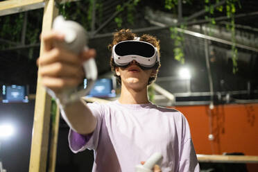 Unten: Ein junger, aufgeregter Mann spielt ein Virtual-Reality-Spiel mit einem VR-Headset und Controllern - ADSF50484