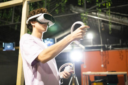 Von unten Seitenansicht des jungen aufgeregten Mannes ist in einer virtuellen Realität Spiel tragen ein VR-Headset und mit Controllern beschäftigt - ADSF50485