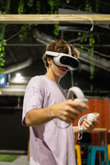 Side view of young excited man is engaged in a virtual reality game wearing a VR headset and using controllers - ADSF50486