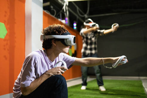 Two young individuals are engaged in an intense virtual reality experience, equipped with VR headsets and controllers at a gaming arcade. - ADSF50489