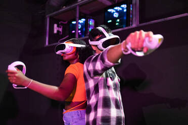 Aufgeregte, gemischtrassige Freunde, die ein Virtual-Reality-Spiel genießen, jeder mit VR-Headset und Controller in der Hand, eingetaucht in ein digitales Abenteuer - ADSF50515