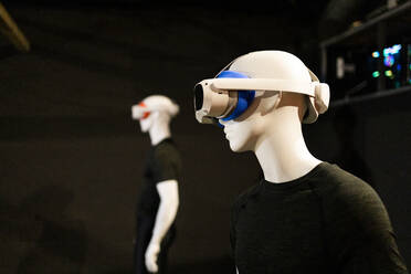 Two futuristic-looking mannequins exhibit VR headsets against a dark, moody backdrop indicative of contemporary technology displays. - ADSF50525