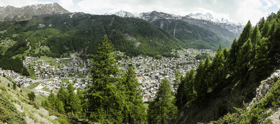Malerischer Blick auf ein Dorf mit Häusern inmitten einer grünen Landschaft und üppigen Bäumen, die auf majestätischen Bergen in der Schweiz wachsen - ADSF50581