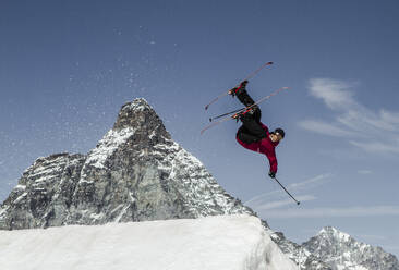 Ganzer Körper eines unbekümmerten aktiven männlichen Skifahrers in warmer Kleidung mit Skiern und Stöcken, der über einen schneebedeckten Berg springt, während er seinen Winterurlaub in den Schweizer Alpen genießt - ADSF50584