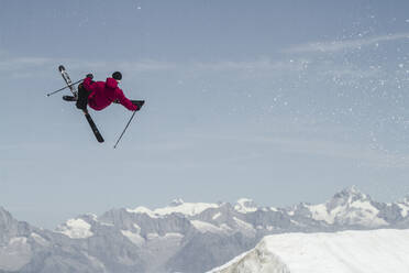 Ganzer Körper eines unbekümmerten aktiven männlichen Skifahrers in warmer Kleidung mit Skiern und Stöcken, der über einen schneebedeckten Berg springt, während er seinen Winterurlaub in den Schweizer Alpen genießt - ADSF50587