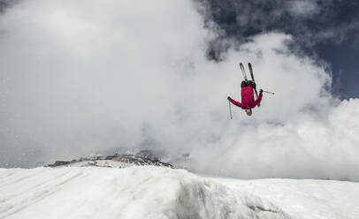 Ganzer Körper eines unbekümmerten aktiven männlichen Skifahrers in warmer Kleidung mit Skiern und Stöcken, der über einen schneebedeckten Berg springt, während er seinen Winterurlaub in den Schweizer Alpen genießt - ADSF50589