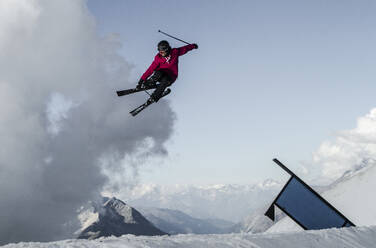 Full body of carefree active male skier dressed in warm clothes with skies and poles jumping above snow covered mountain while enjoying winter vacation at Swiss Alps - ADSF50591