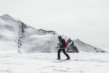 Seitenansicht eines anonymen männlichen Skifahrers in warmer Kleidung mit Rucksack auf Skiern in einer verschneiten Landschaft an einem sonnigen Wintertag in den Schweizer Alpen - ADSF50603