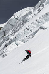 Ganzkörperansicht eines anonymen Mannes mit Snowboard, der über eine schneebedeckte Landschaft mit blauem Himmel in den Schweizer Alpen abfährt - ADSF50610