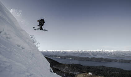 Active unrecognizable person jump ski on snowy covered highland slope against majestic mountains and lake under clear sky in winter vacation - ADSF50619