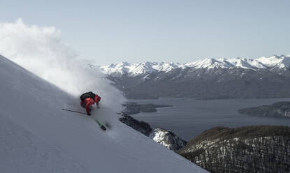 Aktive unerkennbare Person beim Skifahren auf schneebedecktem Hochlandhang gegen majestätische Berge und See unter klarem Himmel im Winterurlaub - ADSF50620