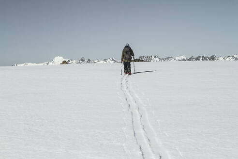 Rückenansicht Ganzkörper von unerkennbaren Person mit Rucksack Skifahren auf schneebedeckten Landschaft unter klaren blauen Himmel während sonnigen Tag im Winterurlaub - ADSF50630