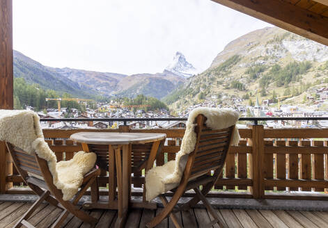 Gemütlicher Balkon mit zwei Sesseln und Blick auf ein malerisches Bergdorf und das berühmte Matterhorn. - ADSF50633