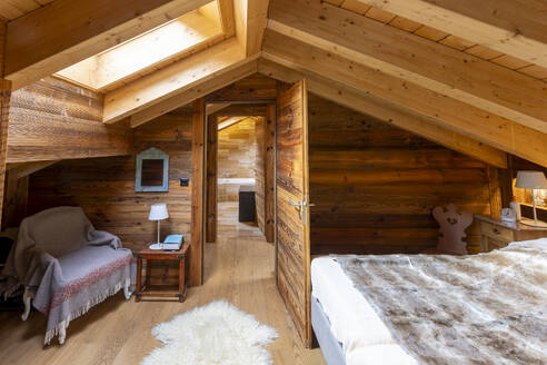A warm, rustic attic bedroom featuring wood-paneled walls, skylight, and comfortable furnishings, for a cozy mountain retreat vibe. - ADSF50634