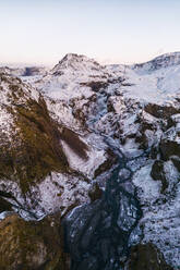 Luftaufnahme des schneebedeckten Thorsmork-Gebirges mit einem gewundenen Fluss, der sich durch zerklüftetes Gelände im isländischen Hochland schlängelt. - ADSF50652