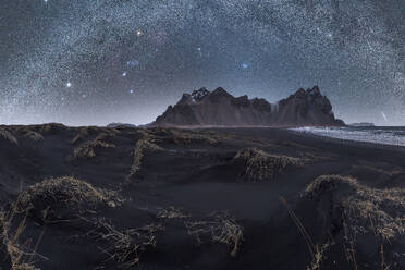 Eine weite Milchstraße leuchtet über einer zerklüfteten Küstenlandschaft mit trockenen Grasbüscheln, die die schwarzen Sanddünen schmücken - ADSF50664